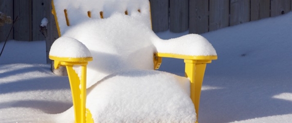 Snow-covered outdoor Adirondack chair illustrating the importance of protecting pool furniture from winter weather and freezing conditions.